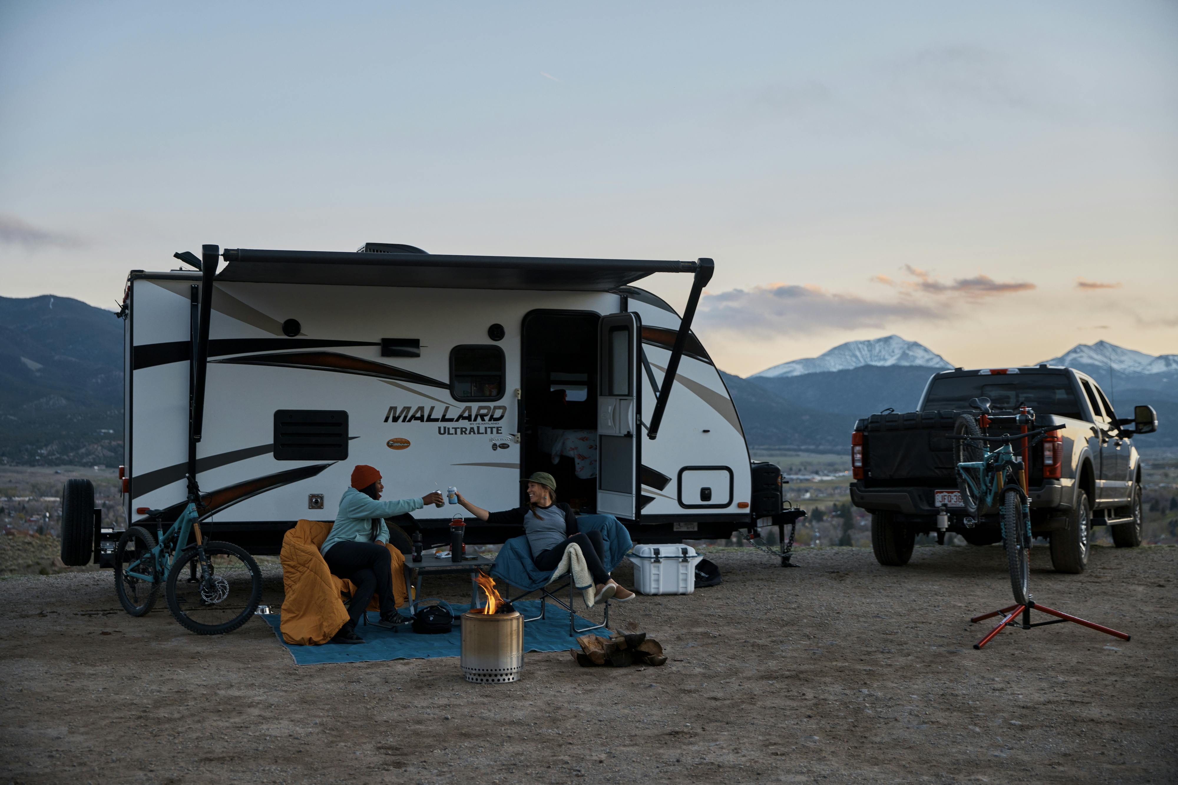 Britt Greer and Brooke Goudy cheers by a fire outside of a Mallard travel trailer