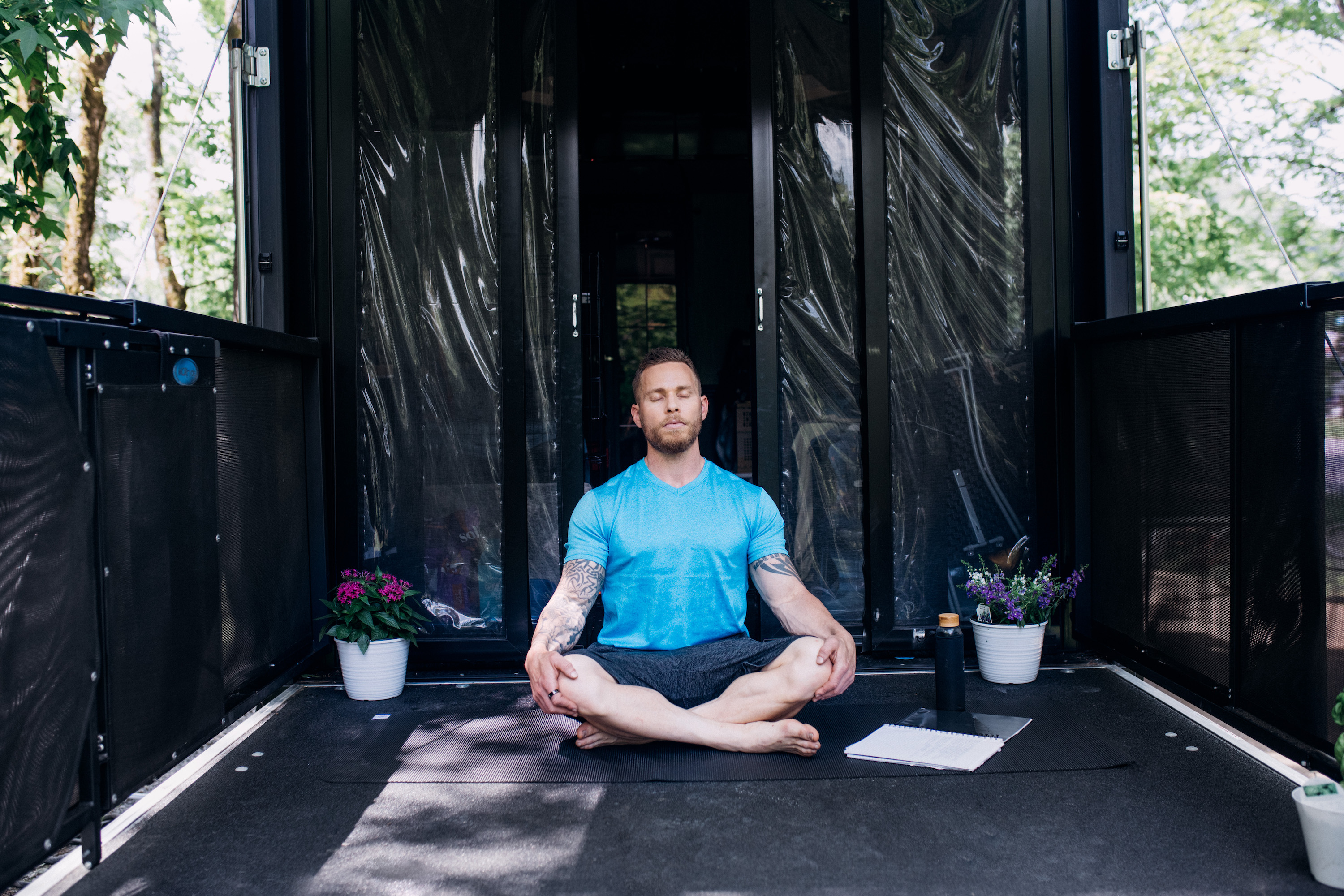 A well-muscled man meditating on the porch of a toy hauler RV.