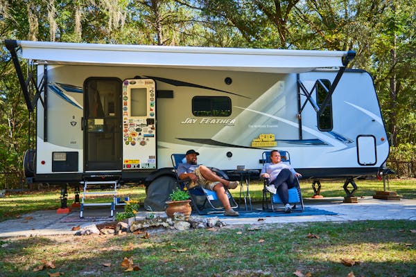 Ben and Christina McMillan lounging in front of their Jay Feather travel trailer