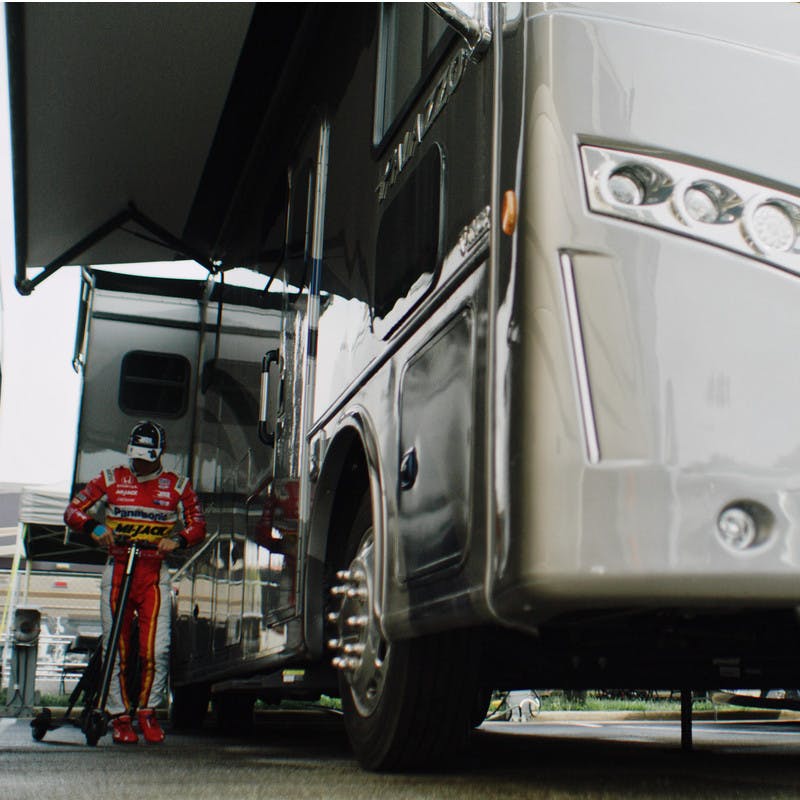 Takuma Sato stands with his scooter next to his Class A Thor Motor Coach RV.