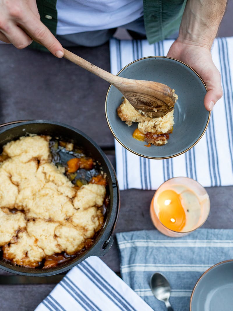 Serving up hot peach cobbler into a bowl with a wooden spoon.
