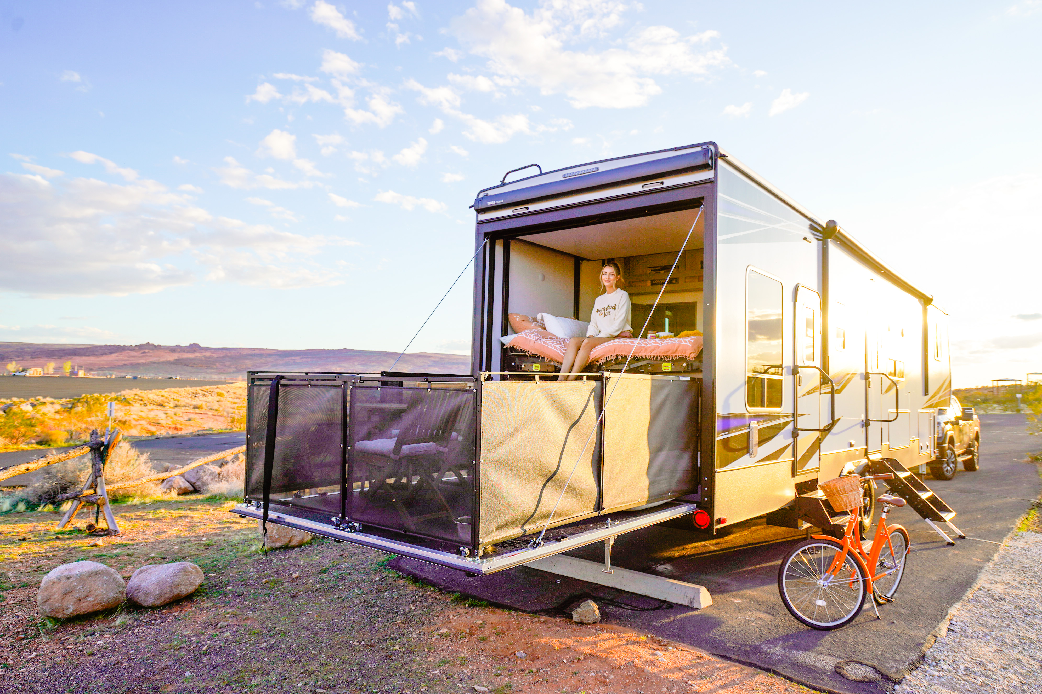 A woman sits on the porch of her toy hauler rv.