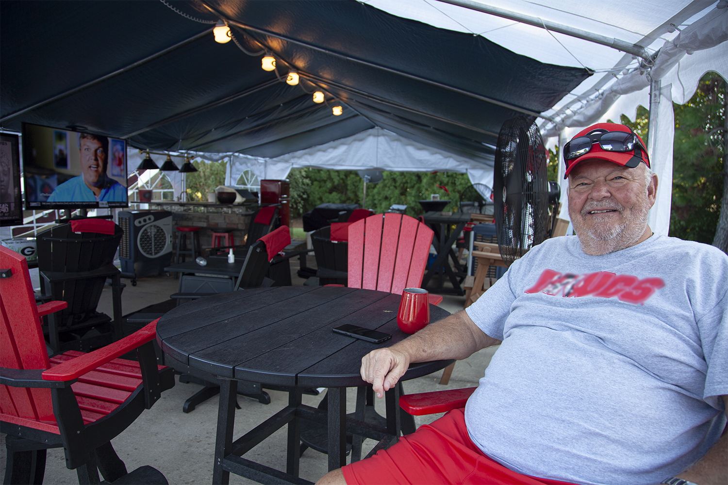 An older gentleman sitting inside of an elaborate tailgating tent, smiling. 