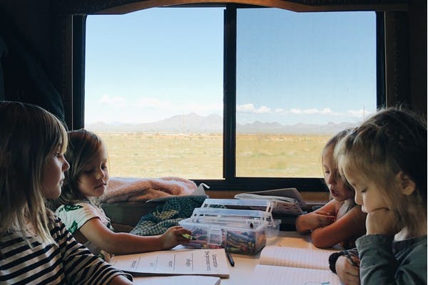 Four young kids sitting at an RV table playing and coloring, with desert mountains out the window.