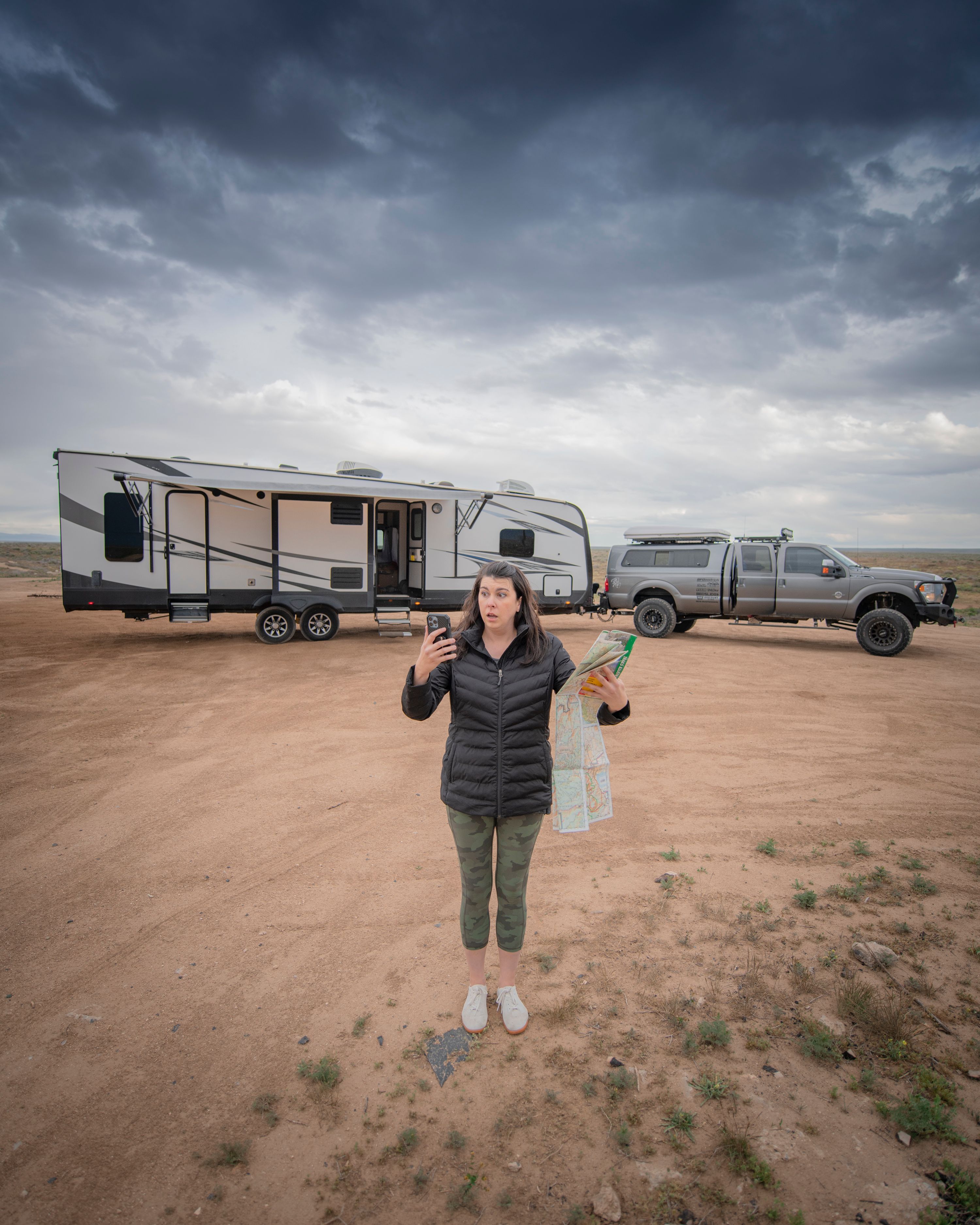 Chelsea Day holding up a map and a phone in front of her travel trailer RV