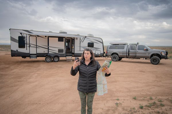 Chelsea Day holding up a map and a phone in front of her travel trailer RV
