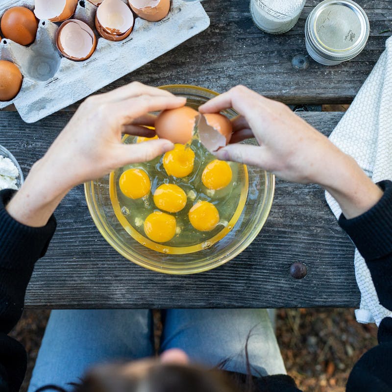Woman cracks egg over glass bowl filled with eggs.
