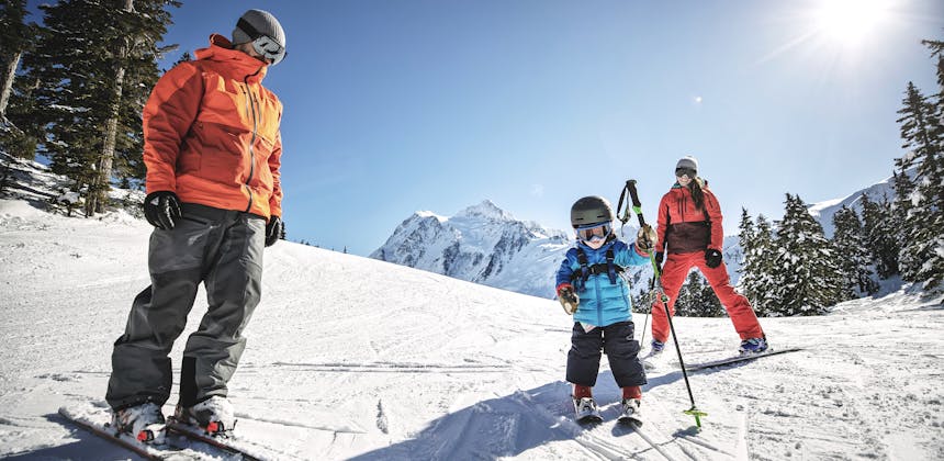 A small child stands on skis with his parents in Mt. Baker, Washington.
