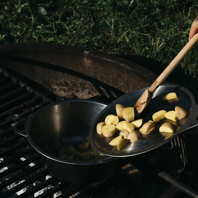 Pushing potatoes into a skillet on a grill to cook. 