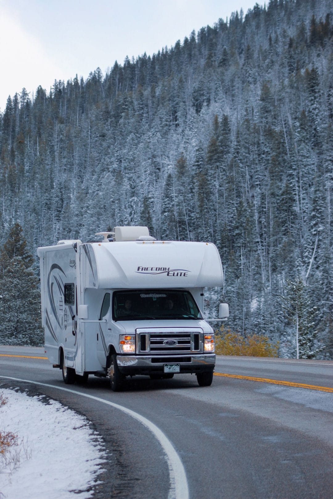 Class C RV drives along windy, snowy mountain road