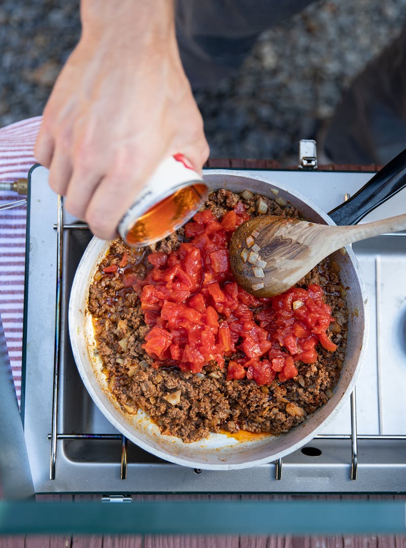 Tomatoes dumped into a pot with ground beef.