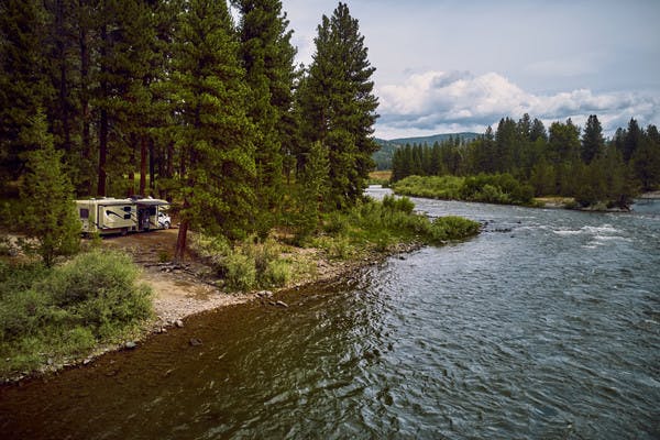 A Class C RV sits next to a bank on the Blackfoot River in Montana.