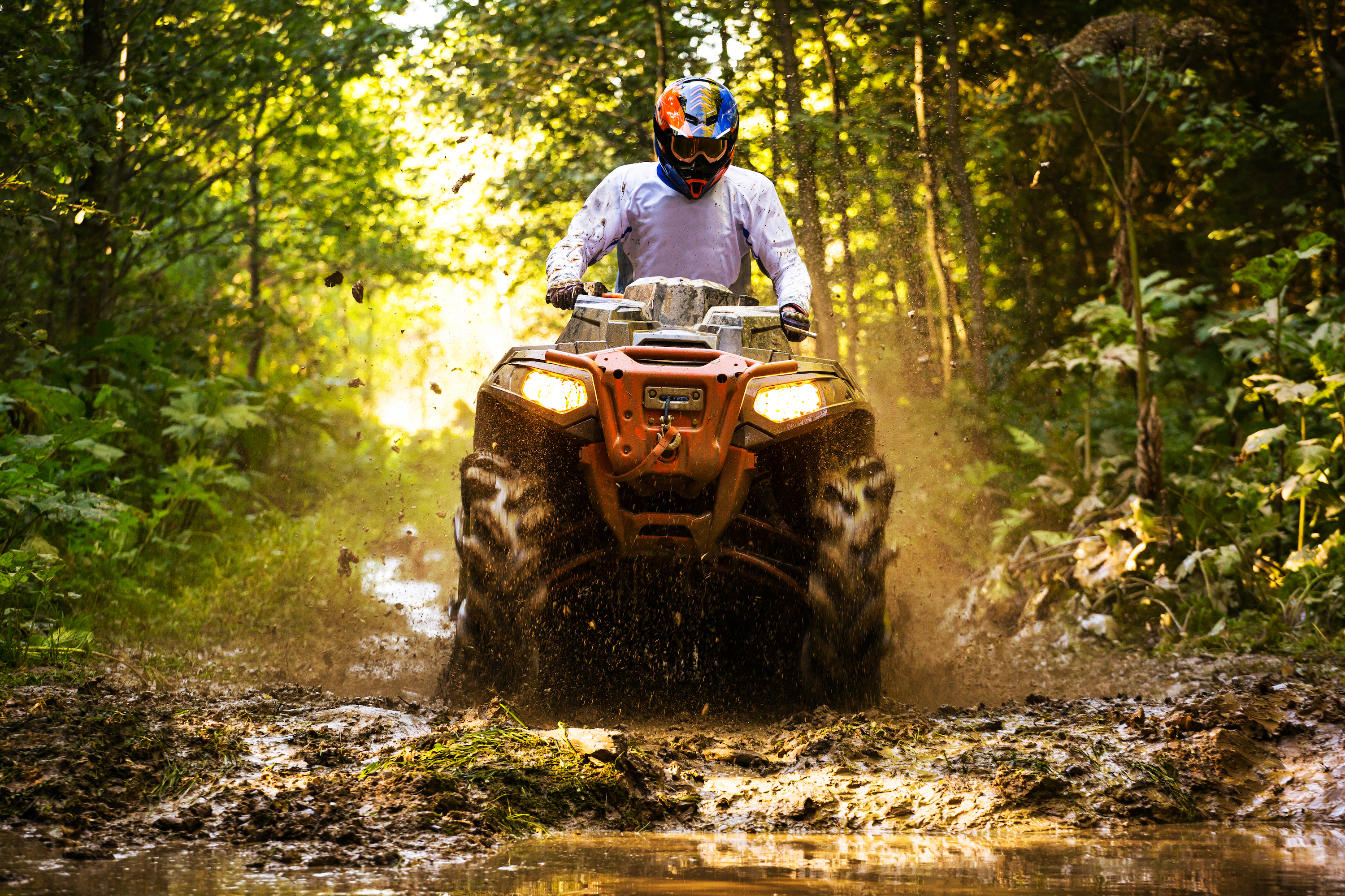 A man ATVs through a muddy forest trail.