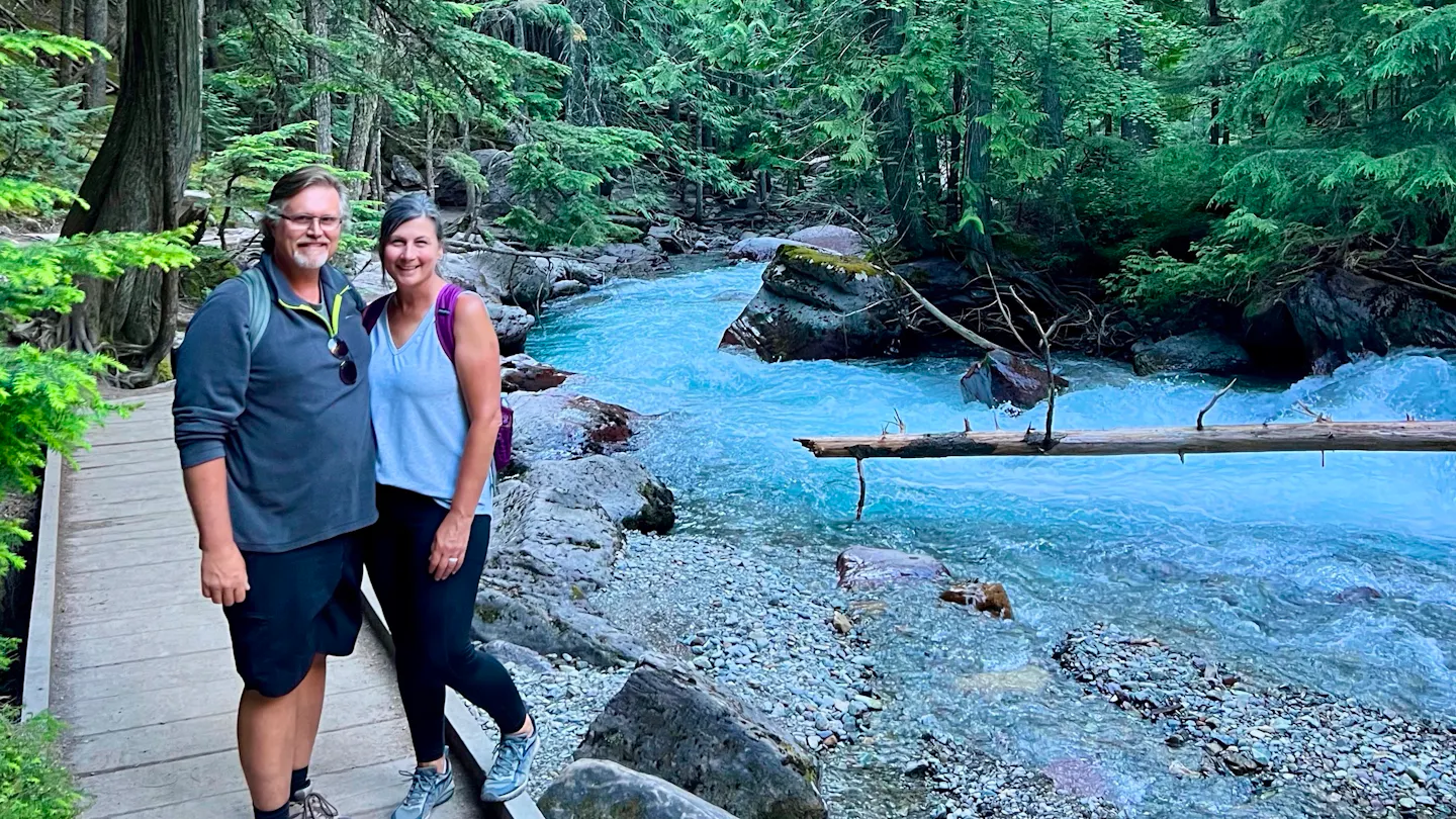 Donny and Tammy Benedict pose on a hiking trail next to a river.