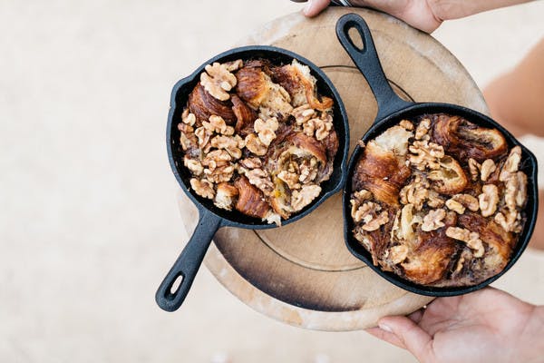 Two mini cast iron skillets on a tray, holding warm caramelized maple walnut croissant pudding.