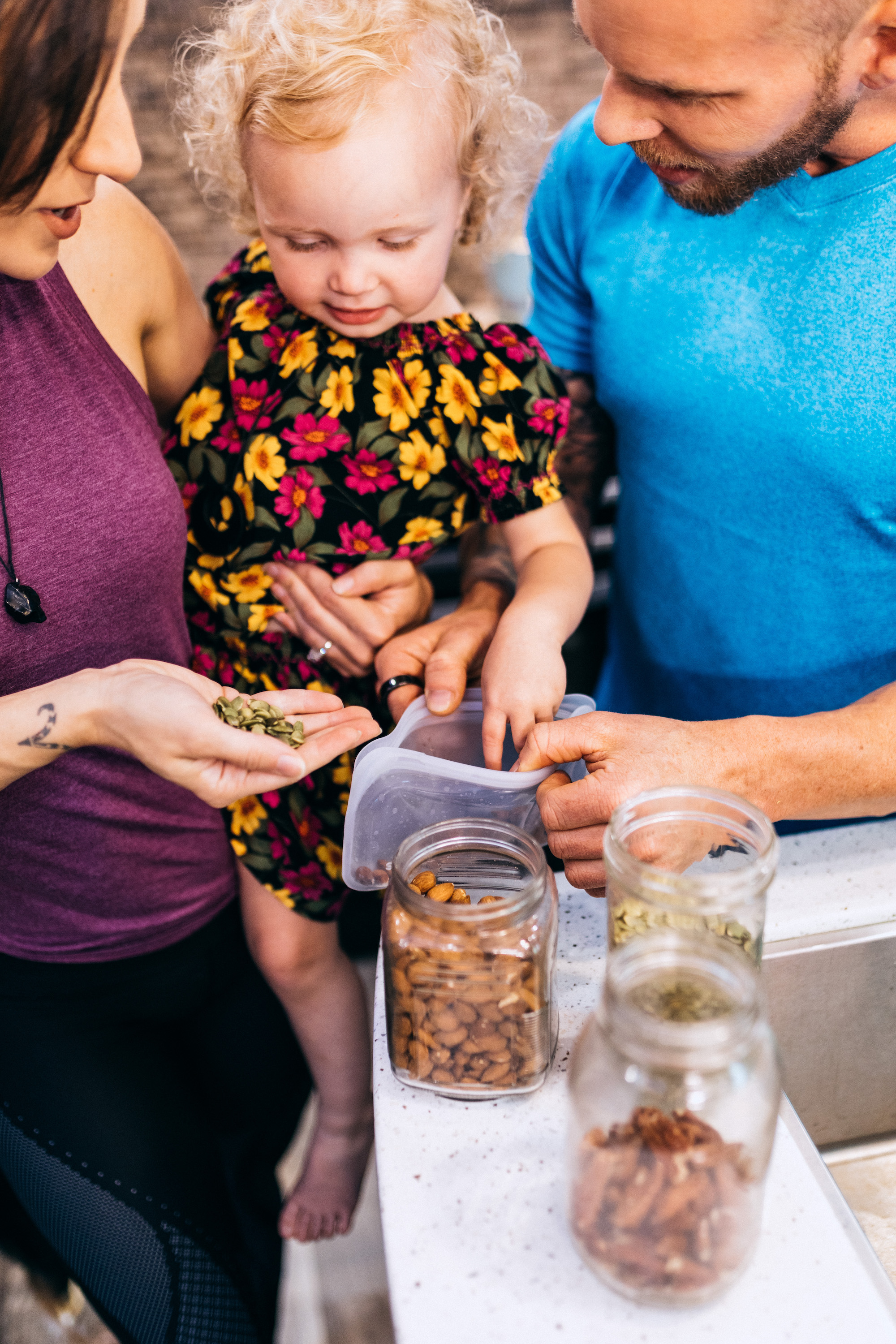 A mom and dad holding their daughter pack seeds and nuts into a baggie as a snack.
