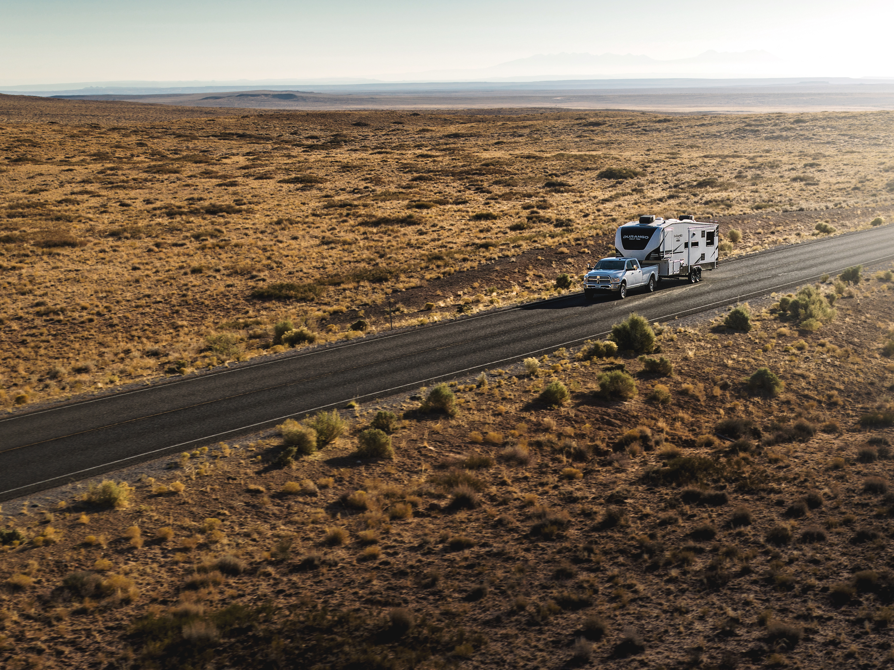 A fifth wheel RV being towed by a truck on a road in the desert.