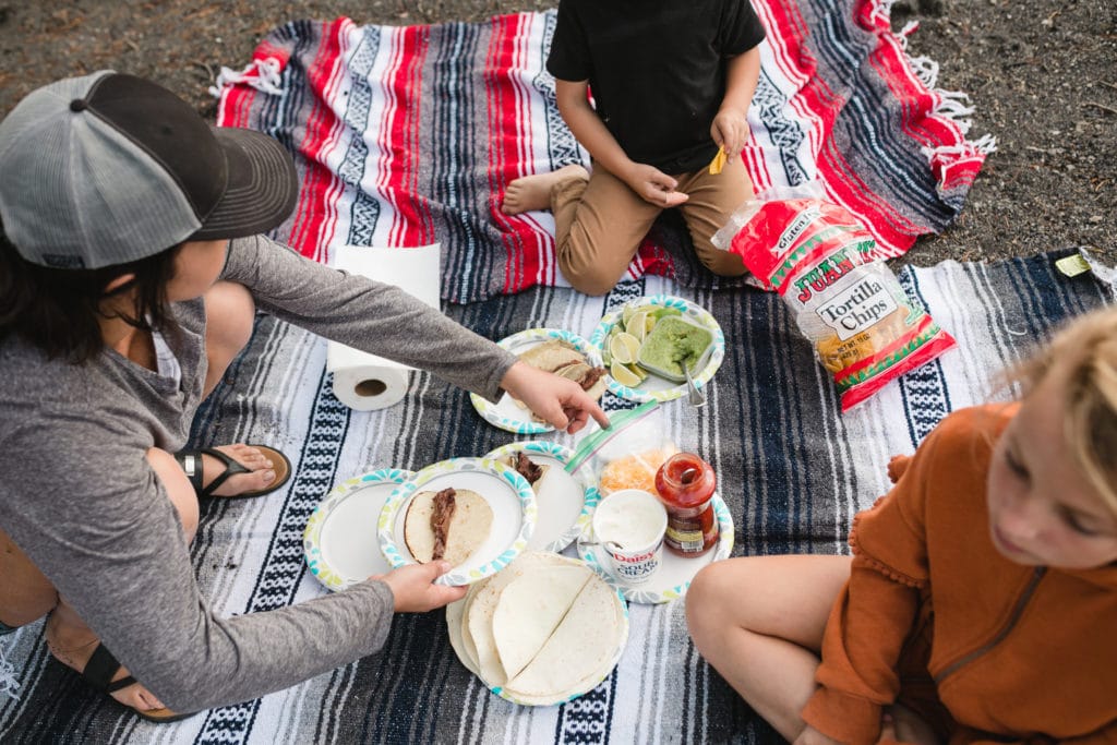 Woman and two kids sit on colorful blankets and assemble tacos