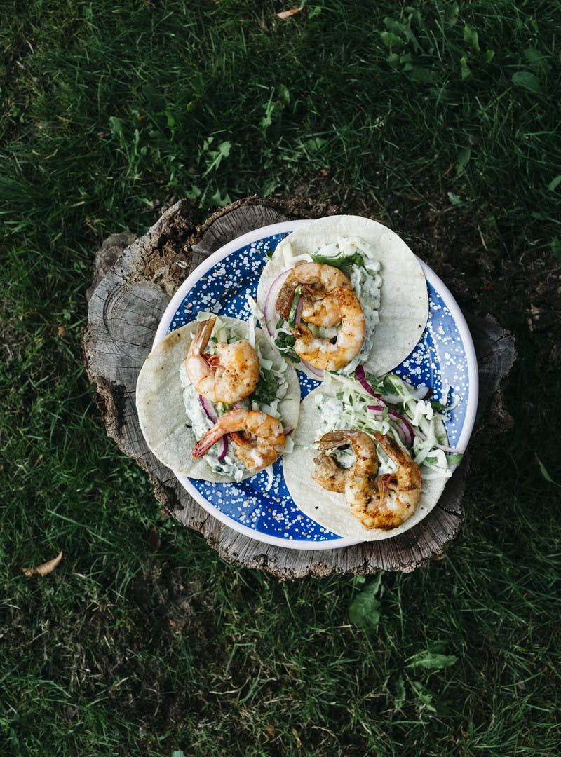 A wider shot of three shrimp tacos assembled with sauce and garnishes.