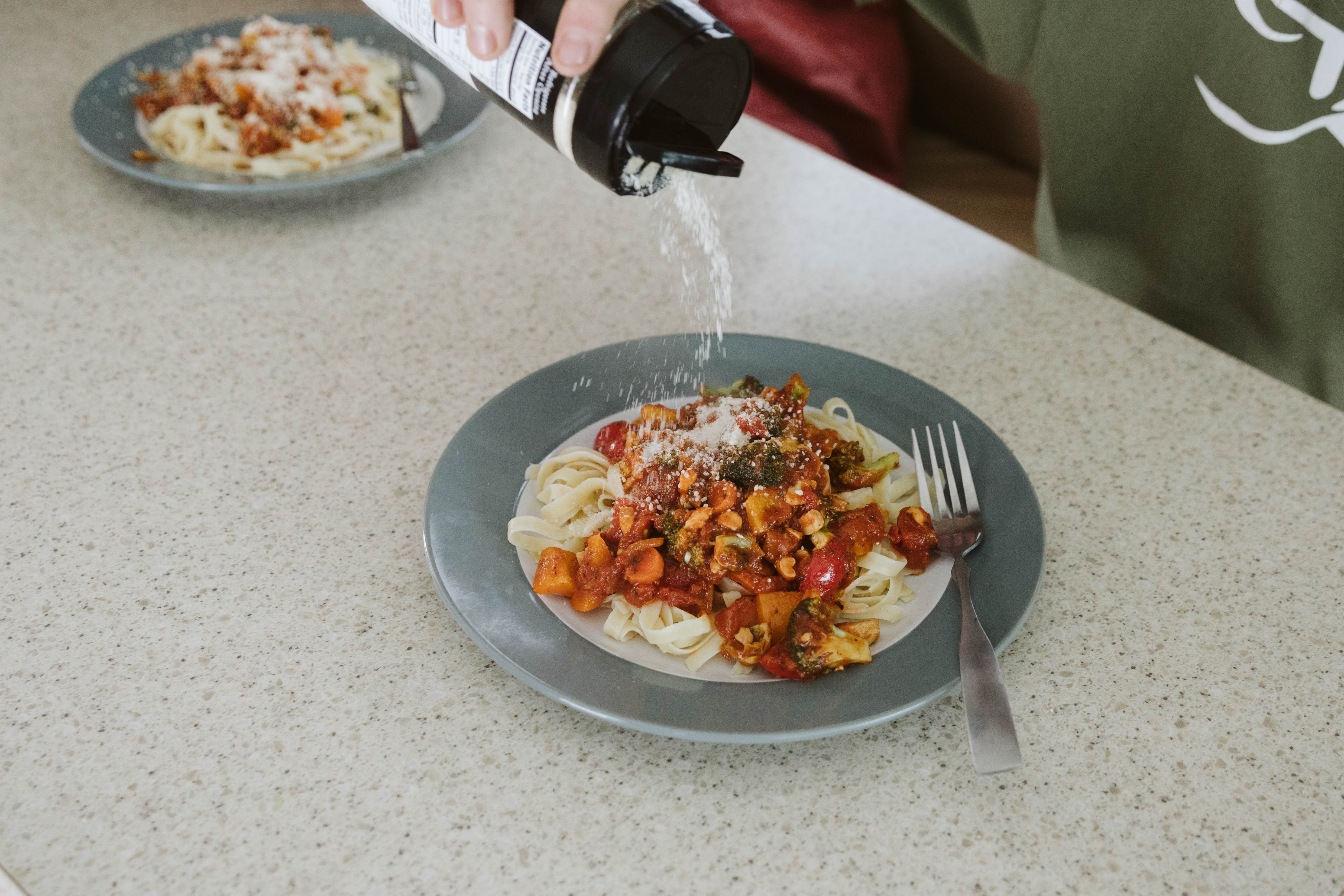A plate of veggie pasta smothered in marinara sauce, veggies and Parmesan cheese. 
