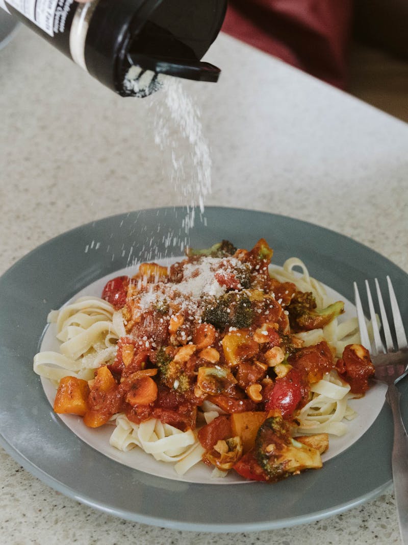 A plate of veggie pasta smothered in marinara sauce, veggies and Parmesan cheese.