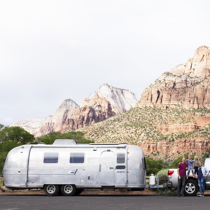 Family standing in front of truck and Airstream travel trailer.  Background includes large rock formations. 