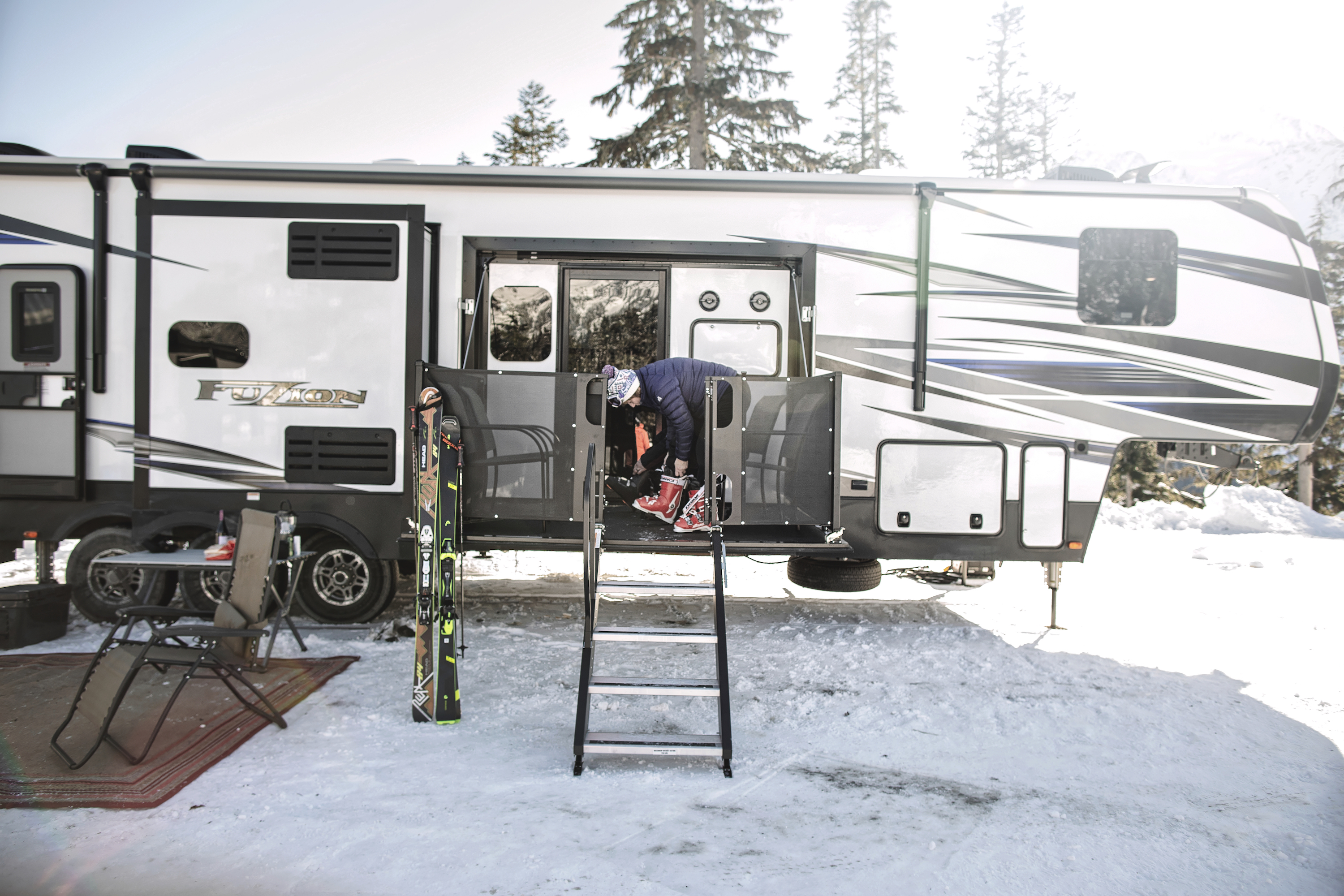 A woman putting on ski boots on the porch of a fifth wheel RV