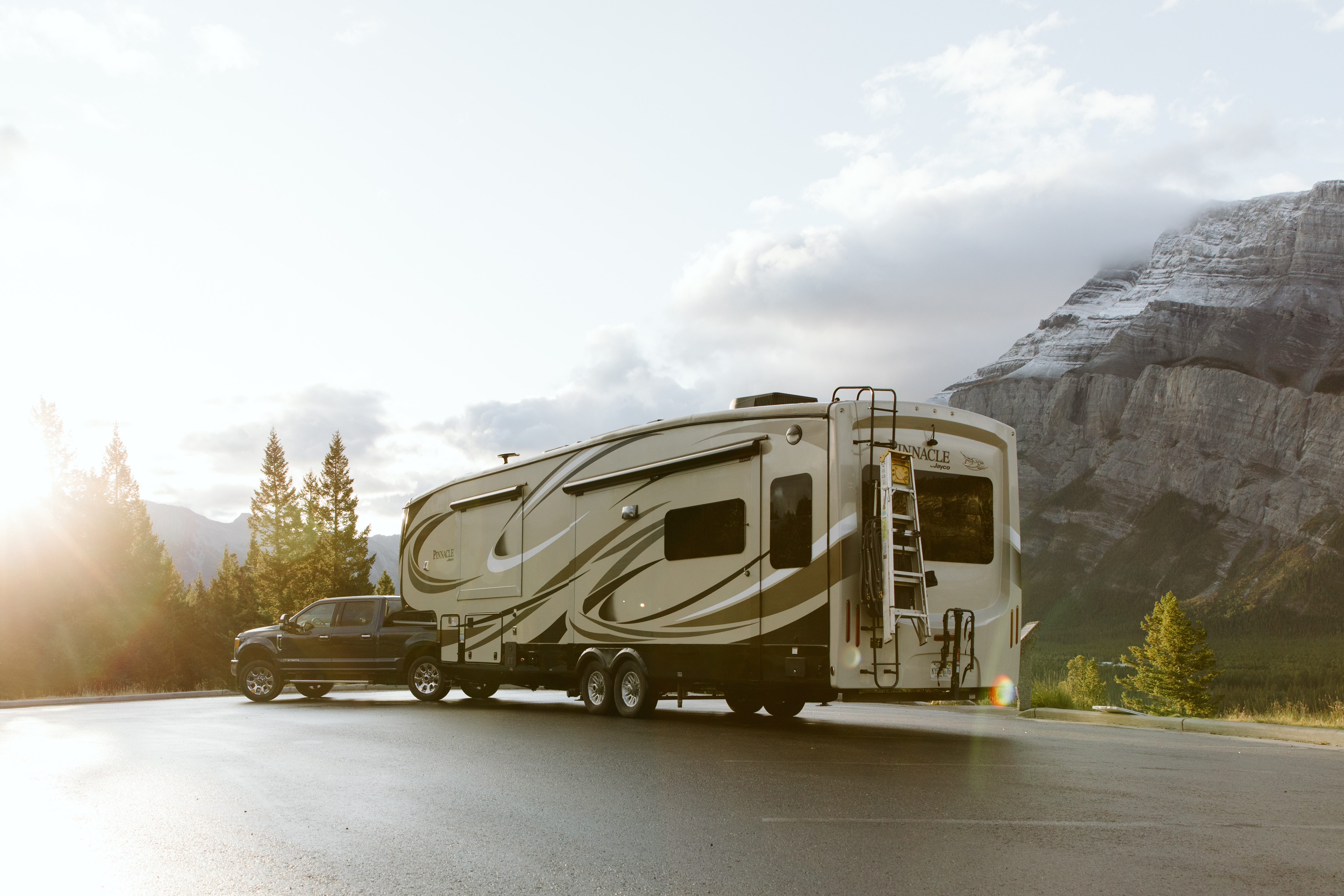 A shot of a truck pulling an RV with mountains in the background and golden light rising on the left. 
