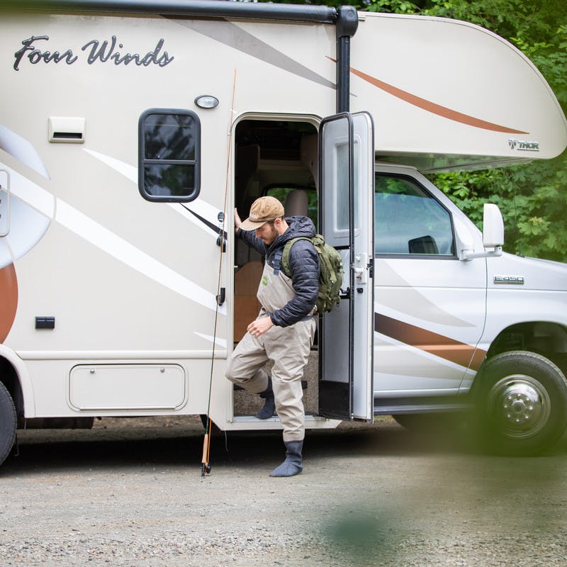 Fisherman with backpack stepping out of Class C motorhome with fishing pole.