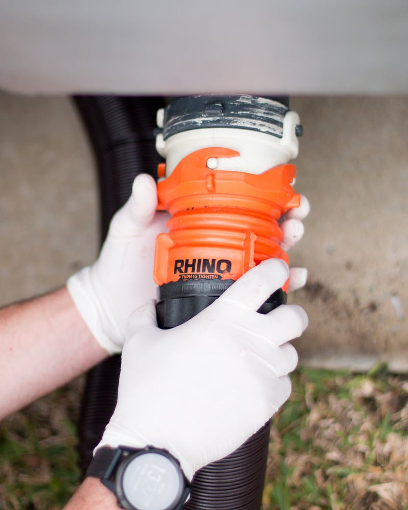 A close up of hands wearing gloves, hooking up the waste hose to the black water tank. 