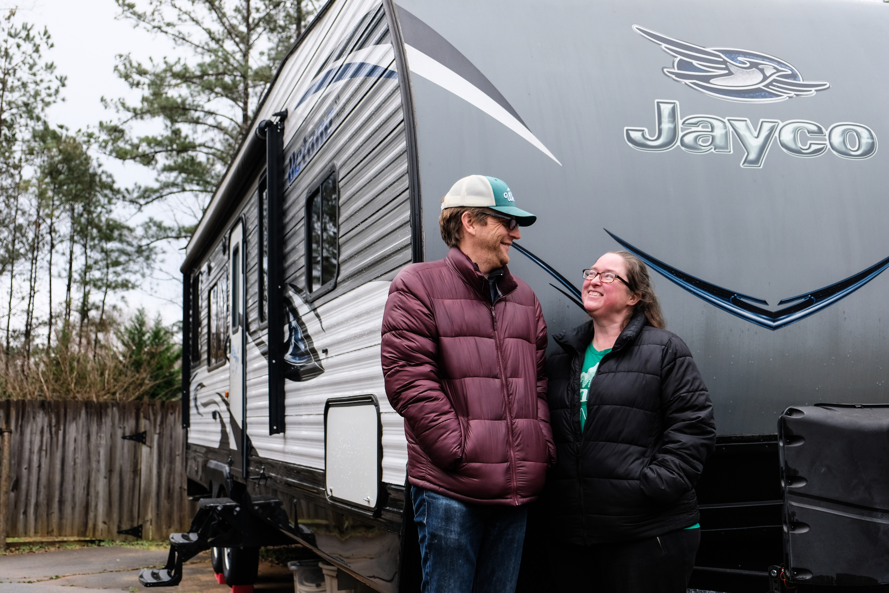 Gretchen Holcomb and her husband smile at each other while they stand in front of their Jayco Octane toy hauler.  