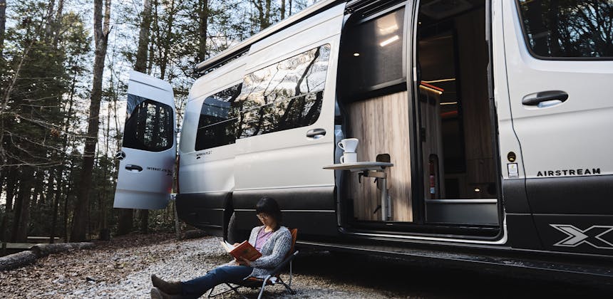 Kathy Karlo reading outside of an Airstream Camper Van