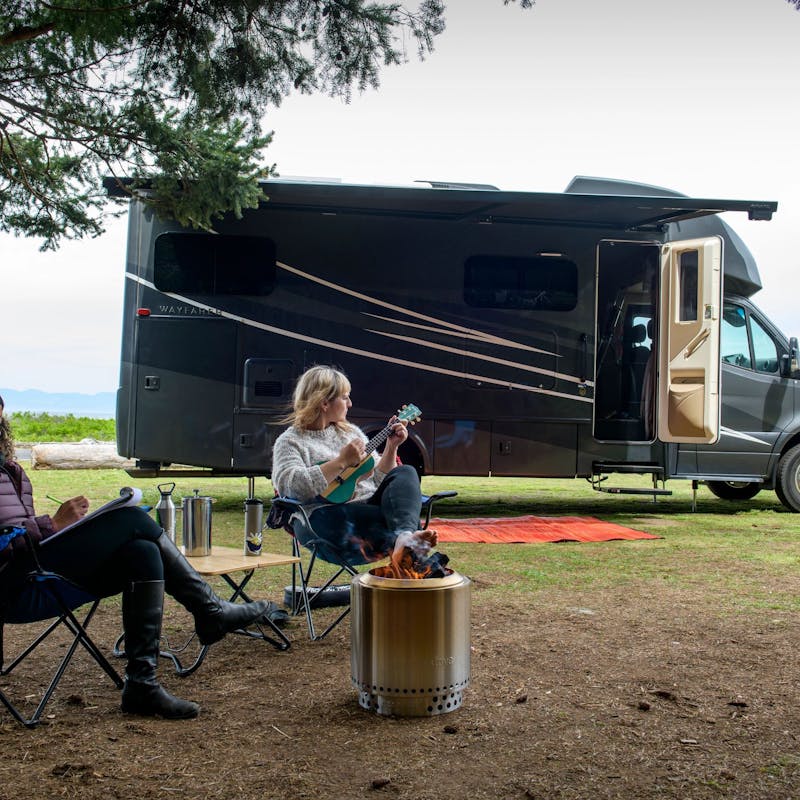 Chelsea and Layla sit together around a fire in front of a Tiffin Wayfarer RV