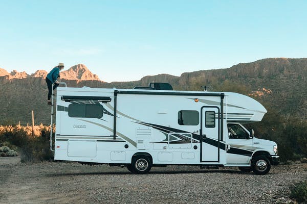Natalie Allen climbing on top of Entegra Class C RV in the desert.