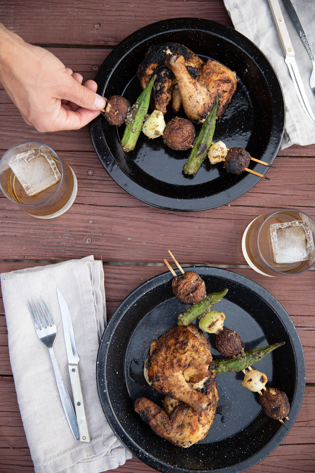 A top down view of two plates holding cooked Cornish hens and okra kabobs. 