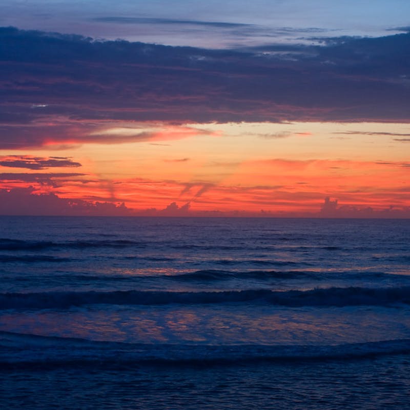 Brilliant pink and orange sunset with purple clouds over the beach with small waves