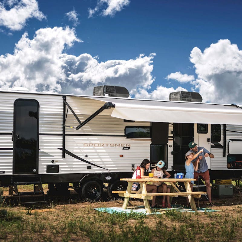 A family sitting outside with a picnic table alongside their KZ RV Sportsmen SE.