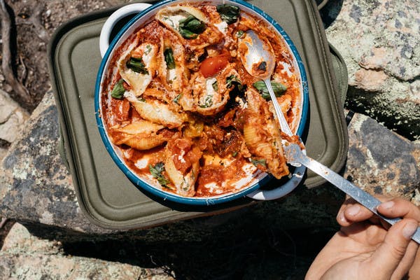 Pasta shells with ricotta cheese, tomatoes, and basil, in a round pan, with a large spoon.