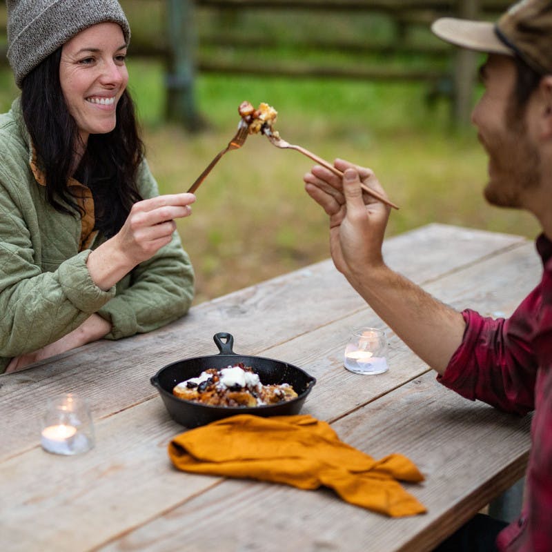 Man and woman wearing hats smile as they cheers their first bite of the banana foster.