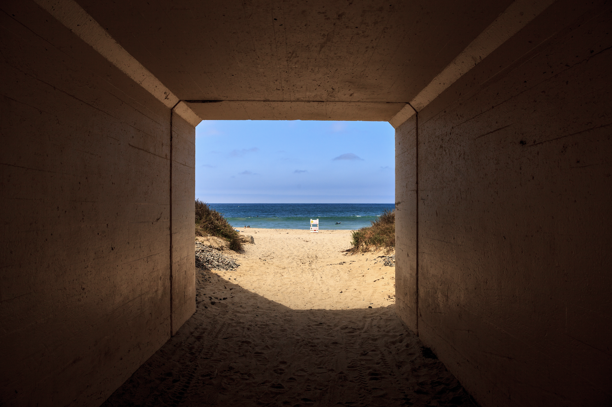 View inside a tunnel looking out at sandy beach, blue ocean and blue sky