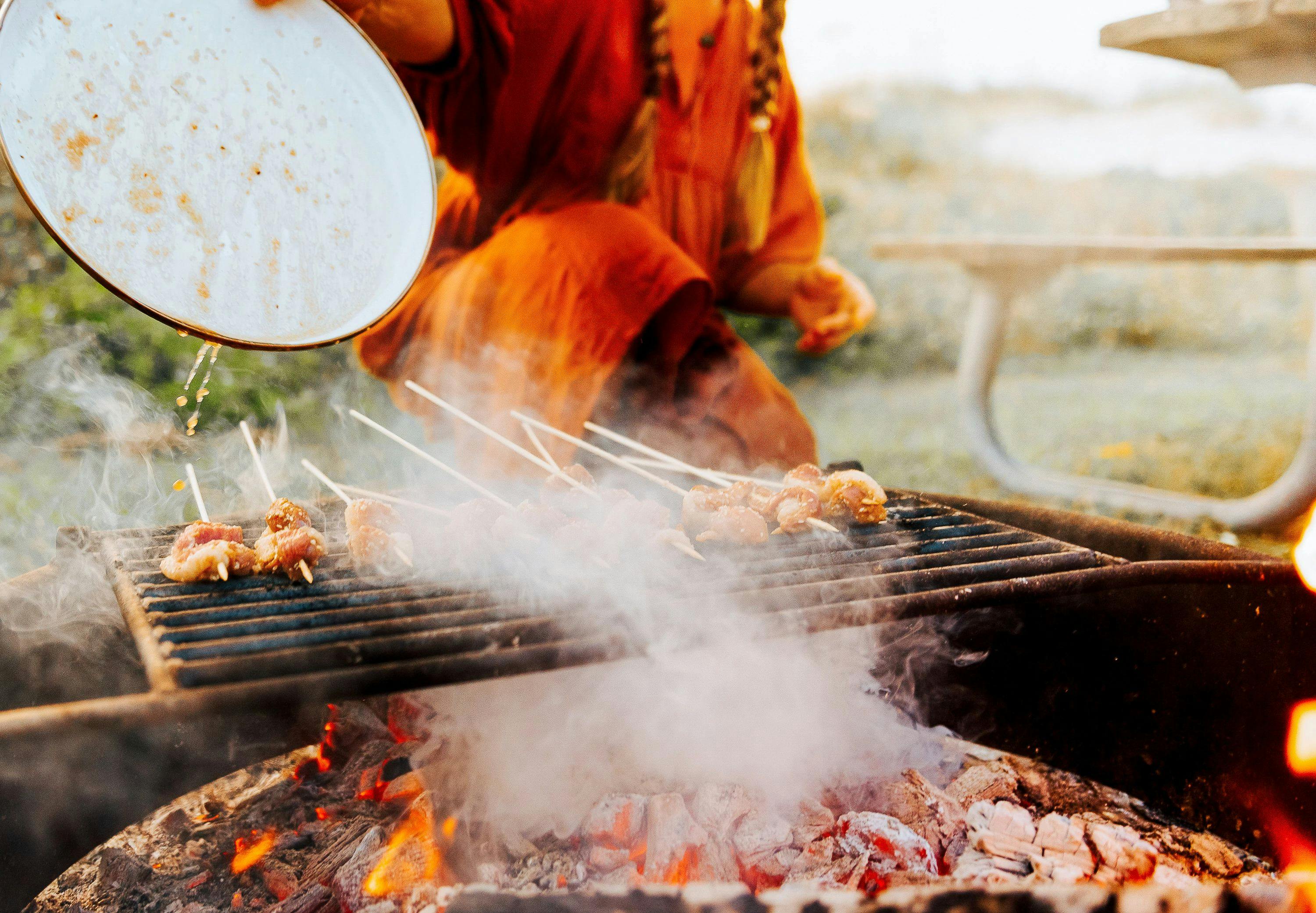 Sarah Glover pouring marinade on top of duck skewers while cooking over an open fire