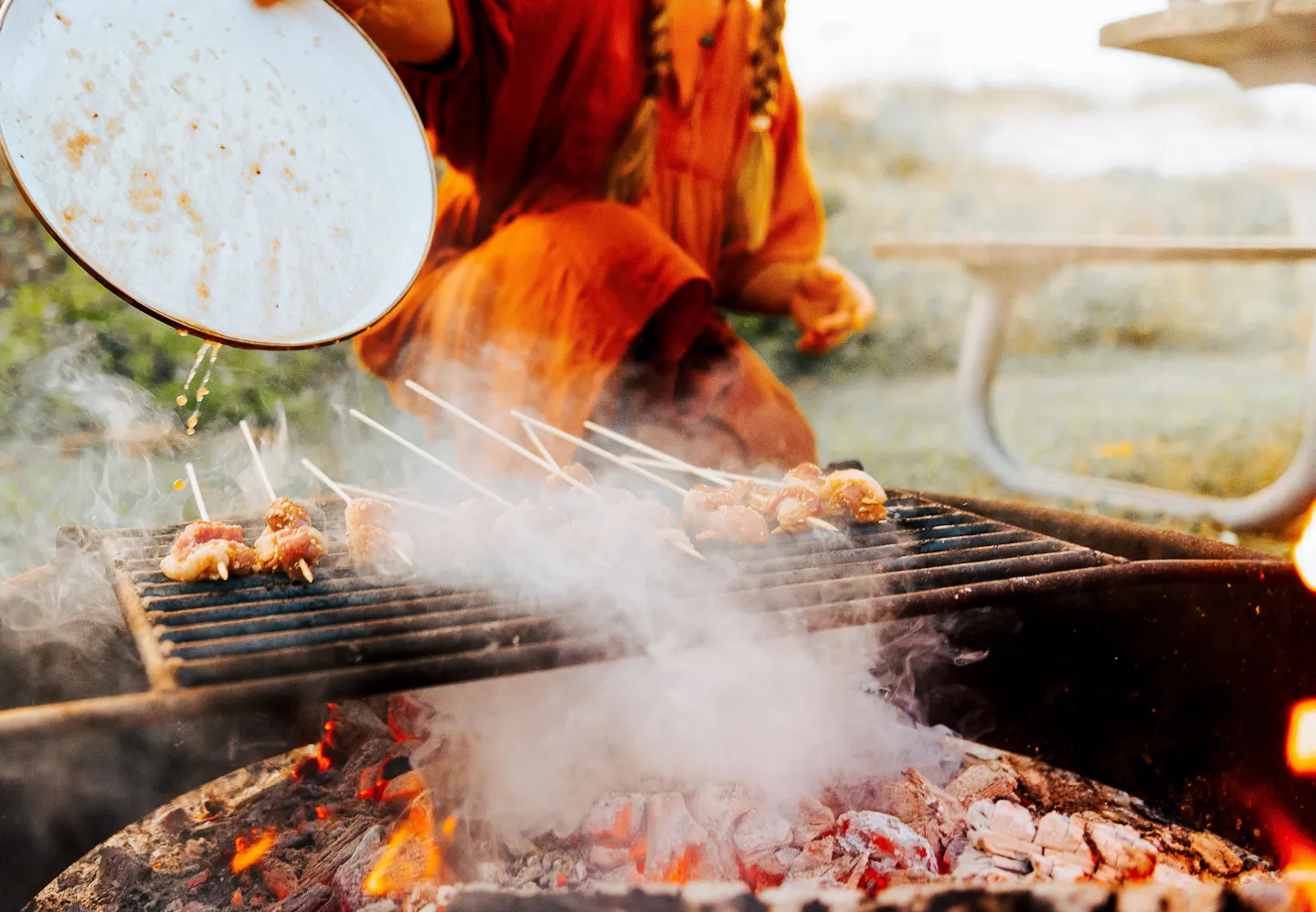 Sarah Glover pouring marinade on top of duck skewers while cooking over an open fire
