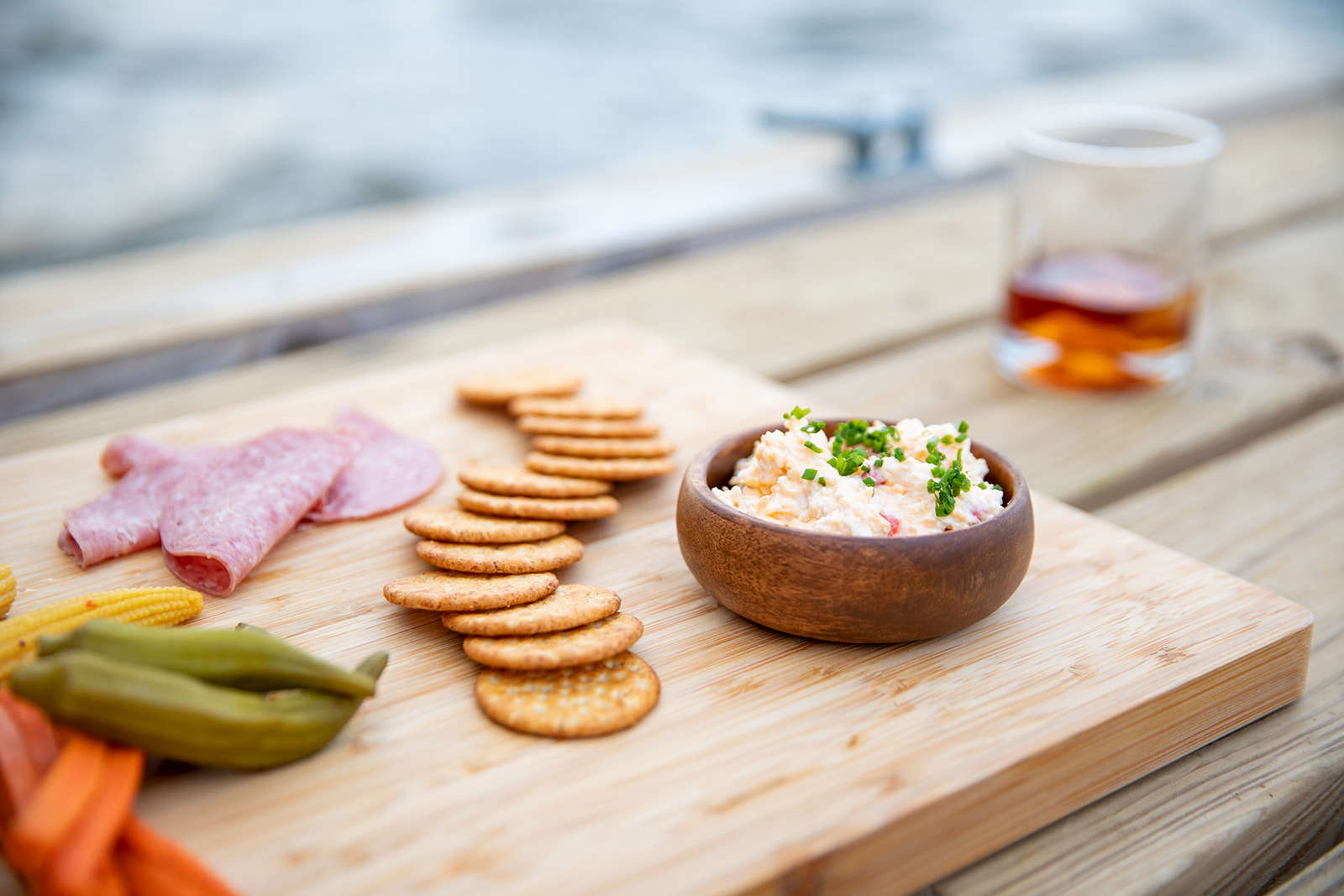 A cheese board with crackers, salami, pickled vegetables and a bowl of pimento cheese spread.