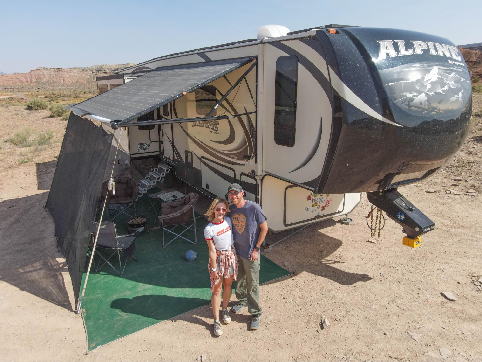 A couple poses in front of their fifth wheel RV