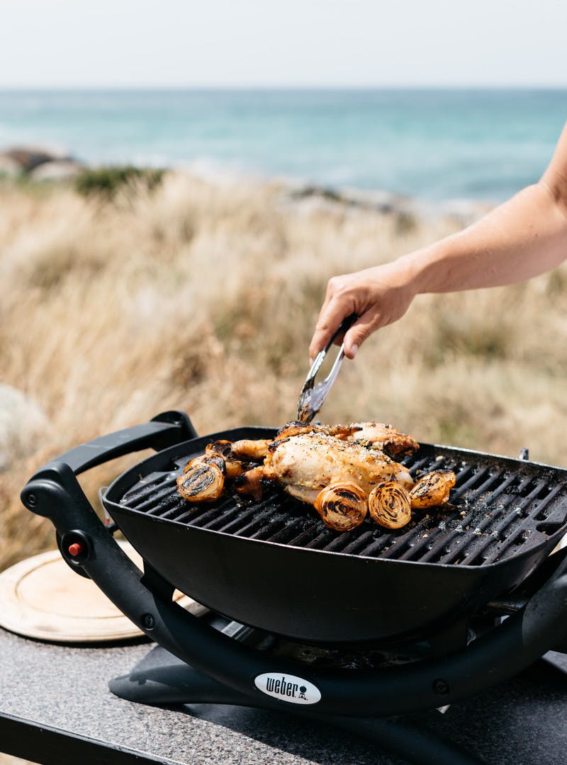 Grilling chicken outside in front of grass and ocean.