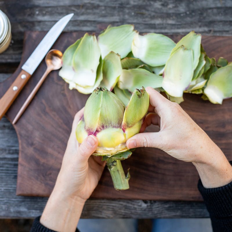 Woman breaks apart artichoke on a cutting board.