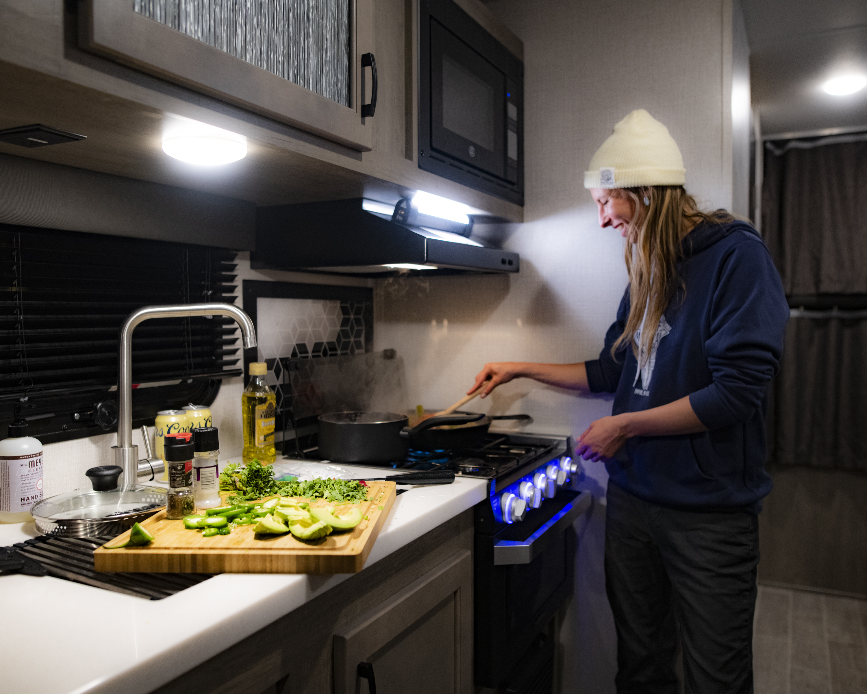 A woman cooks over the stove inside of an RV kitchen.