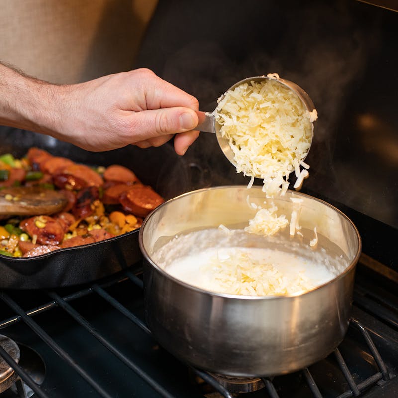 Adding shredded cheese into cooking grits on the stove.