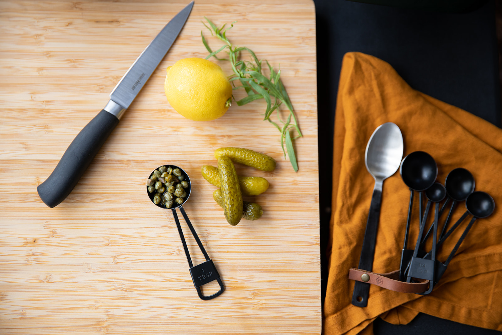 Gherkins, capers, lemon and thyme on a cutting board. 