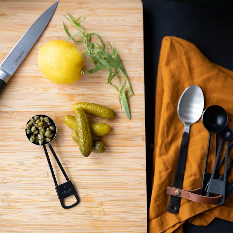 Gherkins, capers, lemon and thyme on a cutting board.